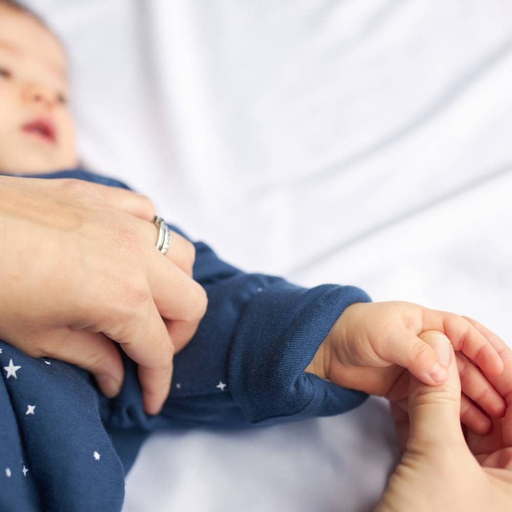 Baby in a blue outfit being held by an adult's hands on a white background