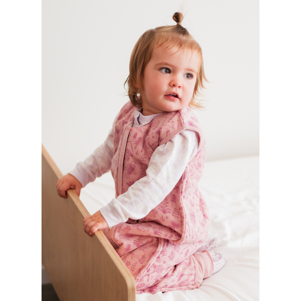 Child in a pink outfit sitting on a bed