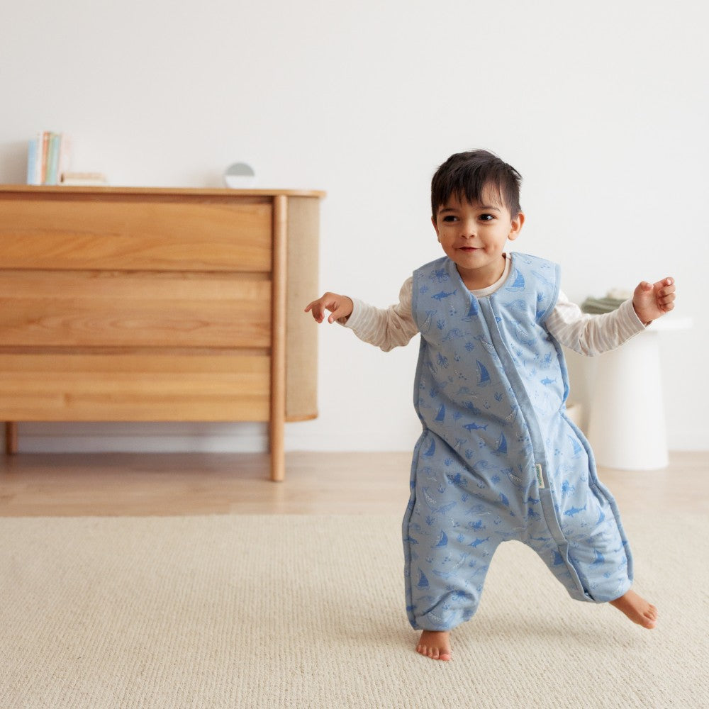 Child wearing a blue patterned onesie in a room with a wooden dresser.