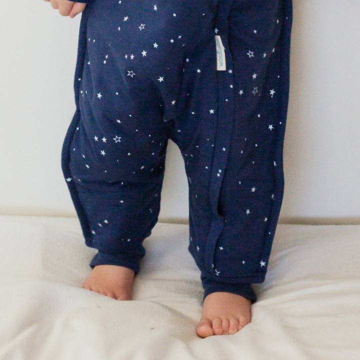Navy blue pajama pants with star pattern worn by a child on a white bed.