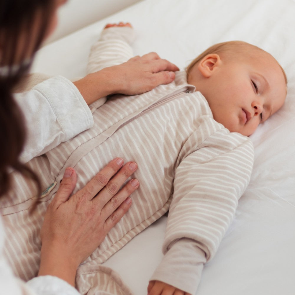 Baby in a striped outfit being comforted by an adult on a white surface