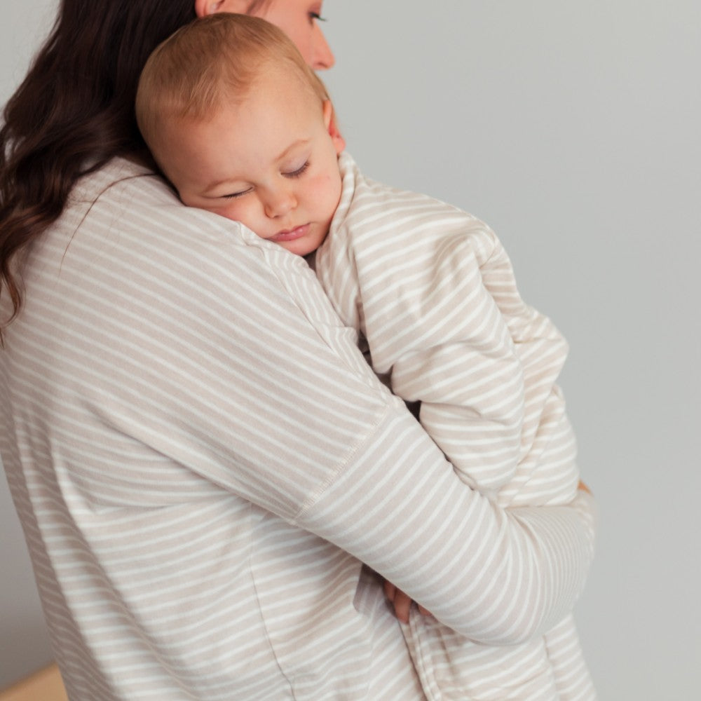 Woman holding a baby wrapped in a striped blanket against a plain background