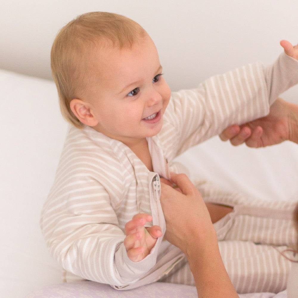 Baby in striped pajamas being helped with a shirt by an adult on a white background