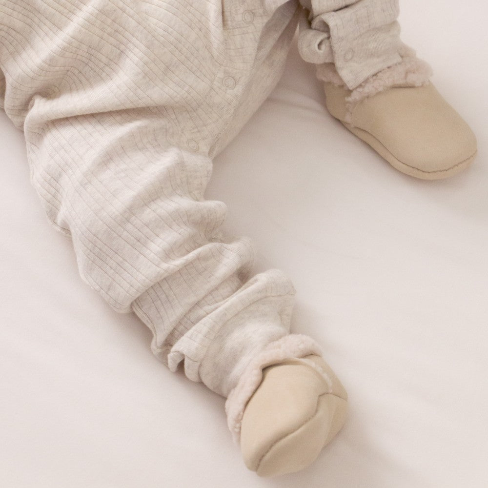 Close-up of baby legs wearing beige pants and shoes on a light background