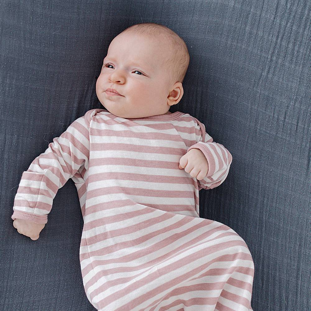 Baby in a pink and white striped prem sized baby gown lying on a textured gray surface
