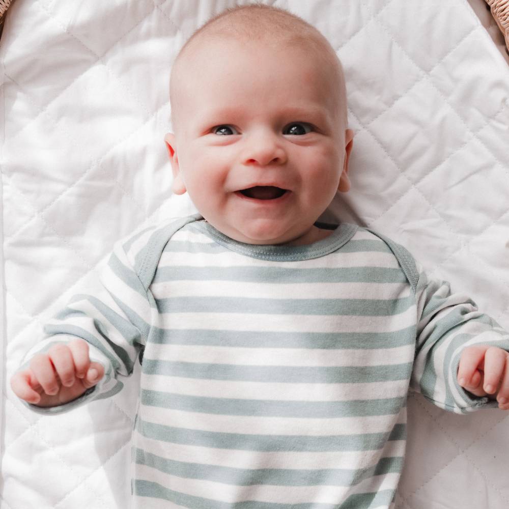 Baby wearing a striped newborn nightgown lying on a quilted surface
