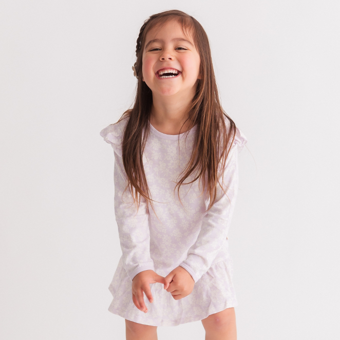 Young girl in a mauve floral nightgown standing against a plain background