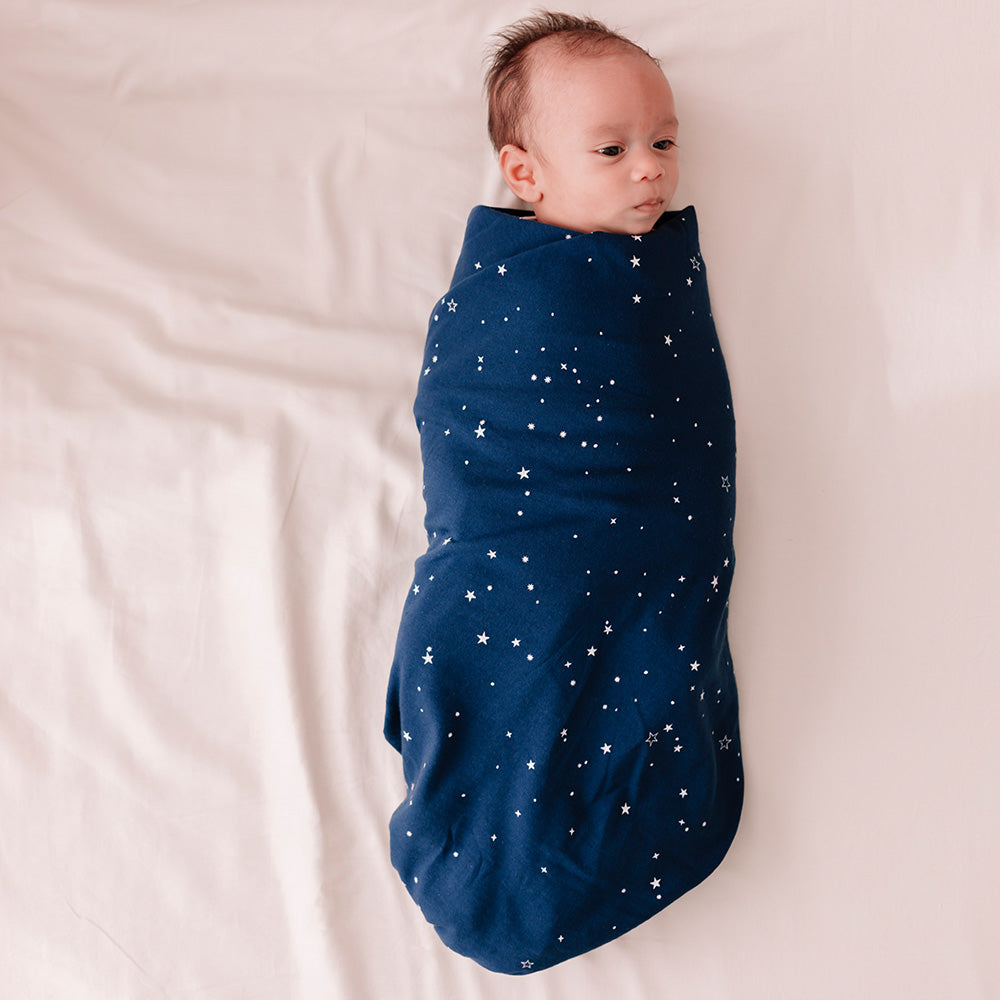 Baby swaddled in a navy blue blanket with star patterns on a light pink background