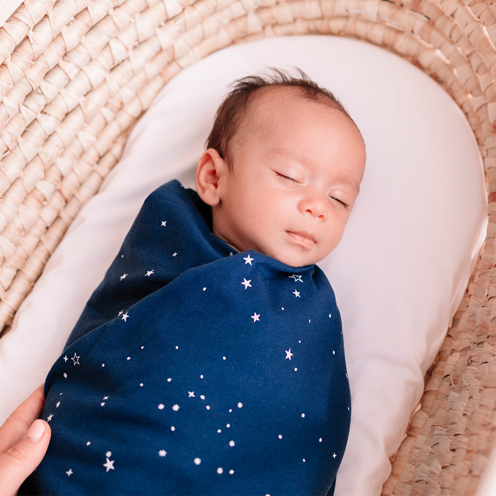 Newborn baby swaddled in a blue blanket with star patterns, lying in a woven basket.