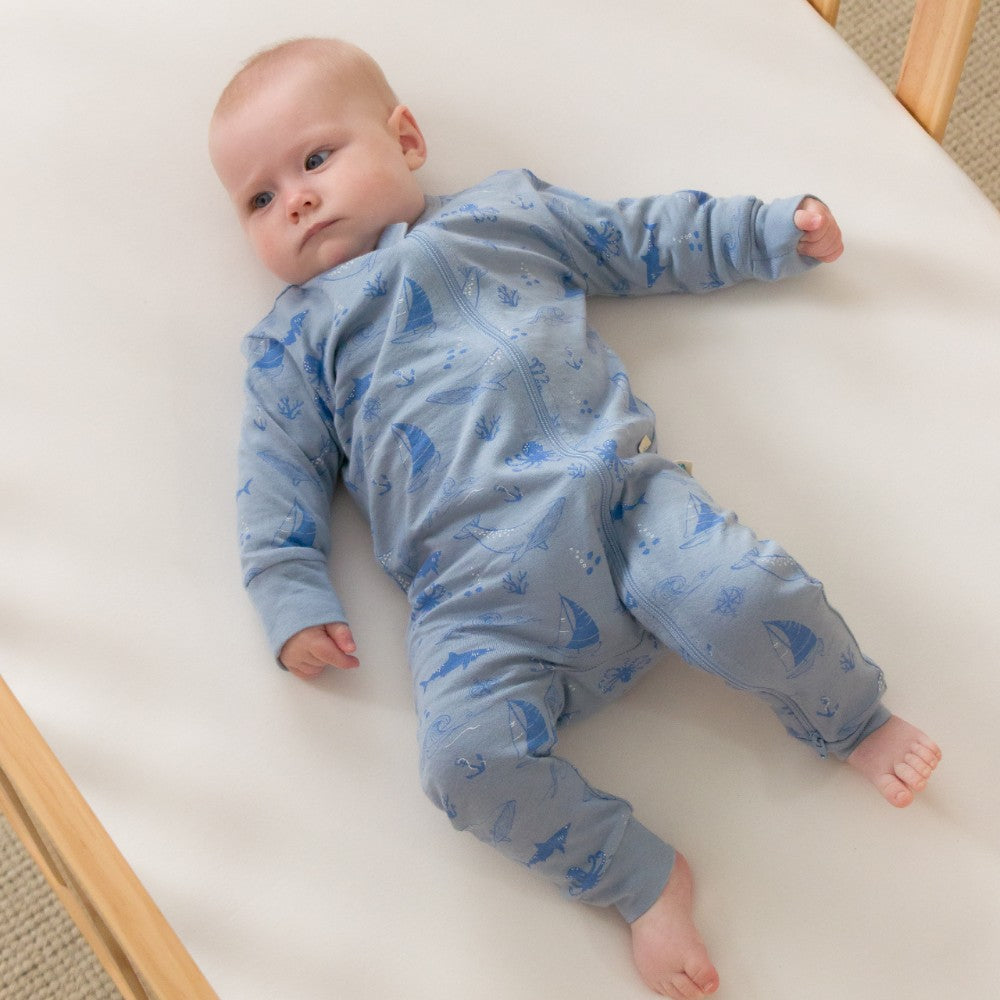 Baby wearing a blue onesie with whale pattern lying on a white crib.
