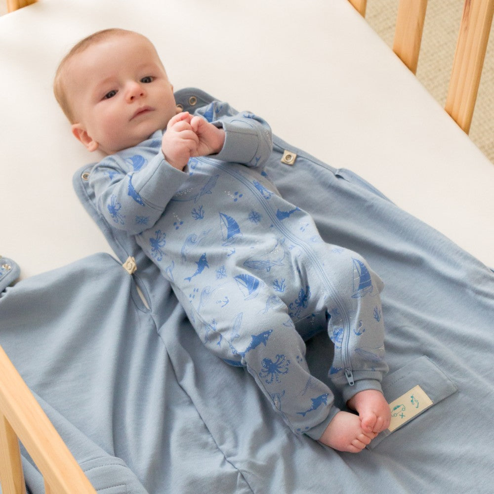 Baby in a blue onesie with animal prints lying on a crib.