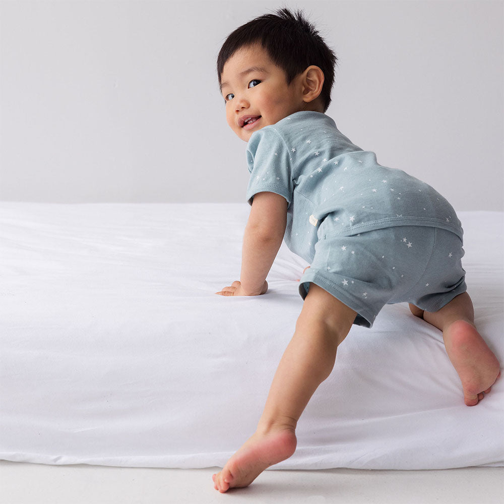 Baby in light blue outfit standing on a white surface