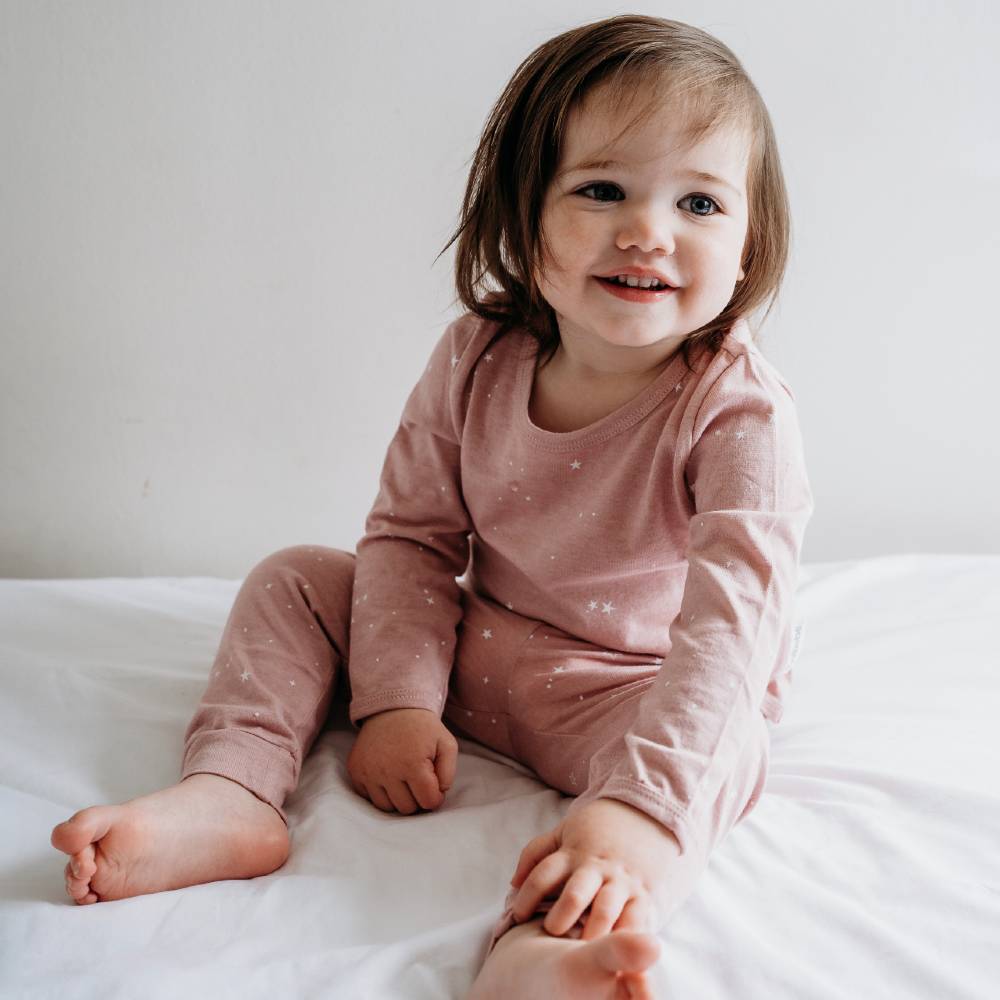 Child wearing pink pajamas sitting on a white bed