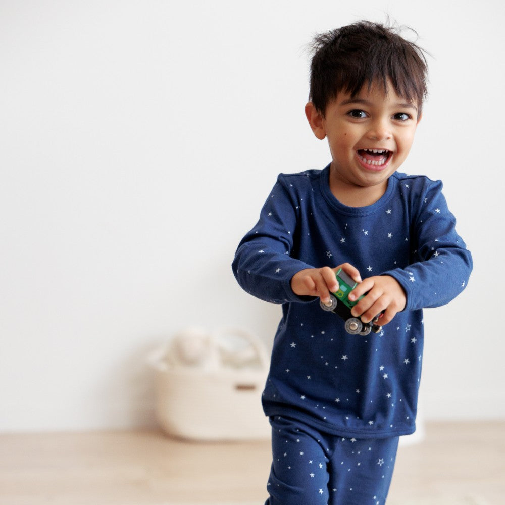 Child wearing a blue pajama set with star pattern, holding a toy car indoors.