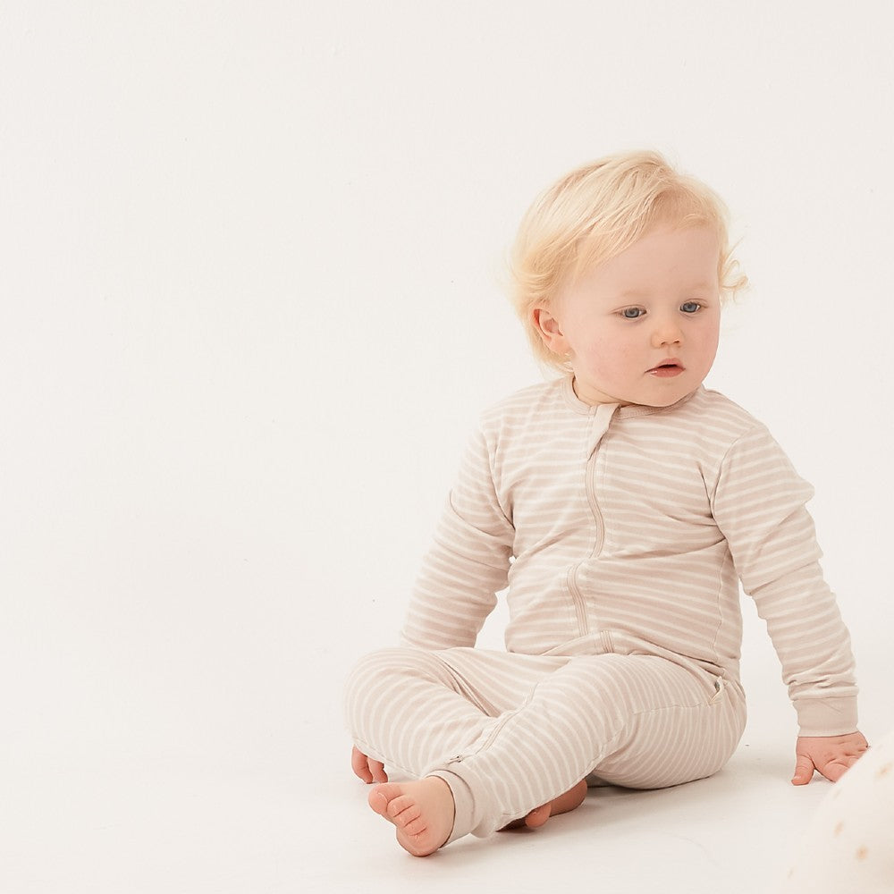 Baby wearing a beige ribbed onesie sitting on a white surface.