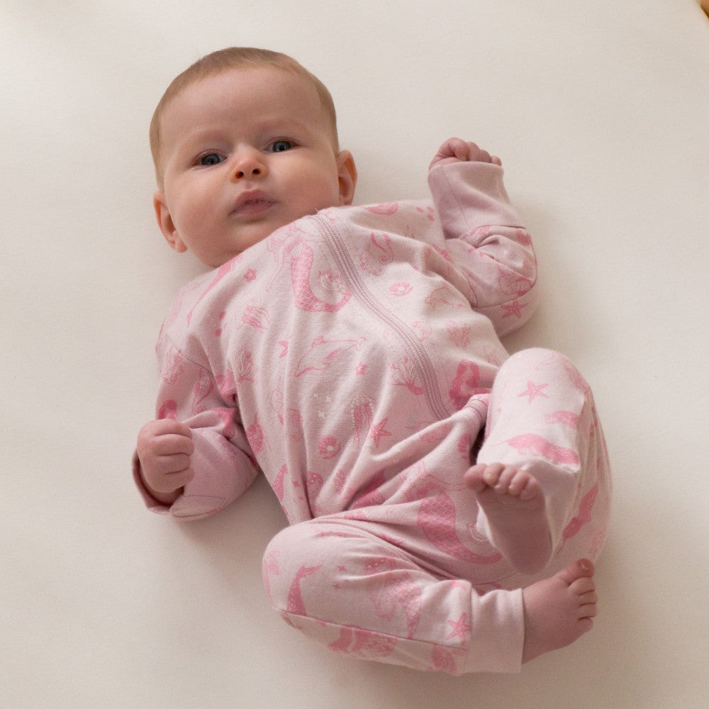 Baby wearing a pink onesie with a pattern, lying on a white surface