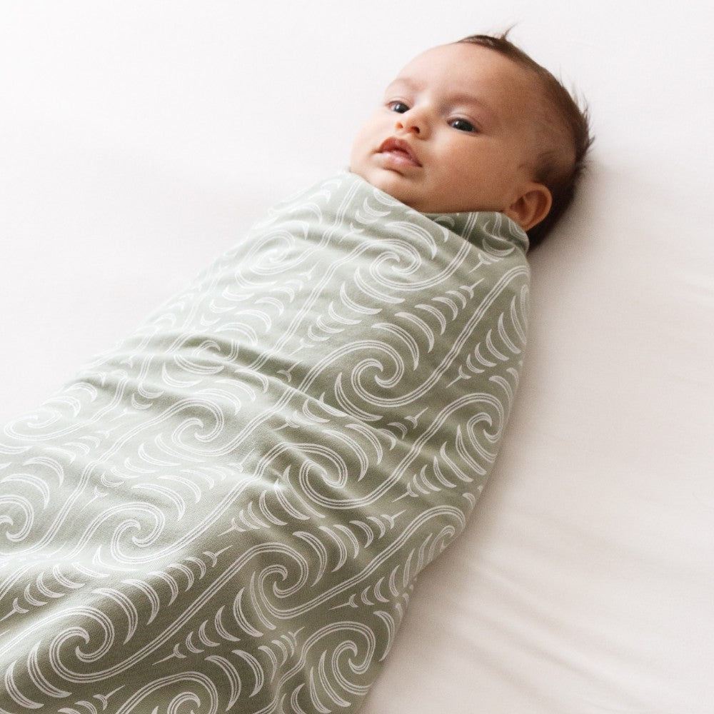 Baby swaddled in a Maori patterned blanket on a white surface