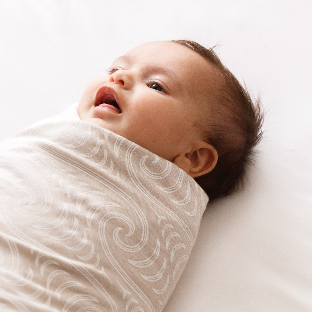 Baby wrapped in a Maori patterned merino swaddle on a white background