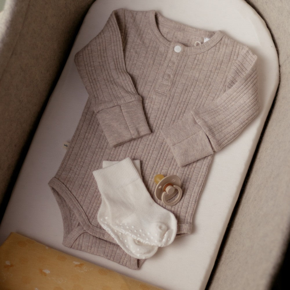 Baby outfit with cardigan, socks, and pacifier on a white surface