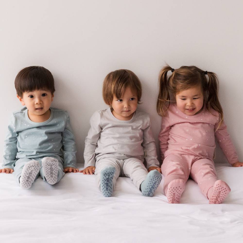 Three children sitting on a white bed wearing matching pajamas.