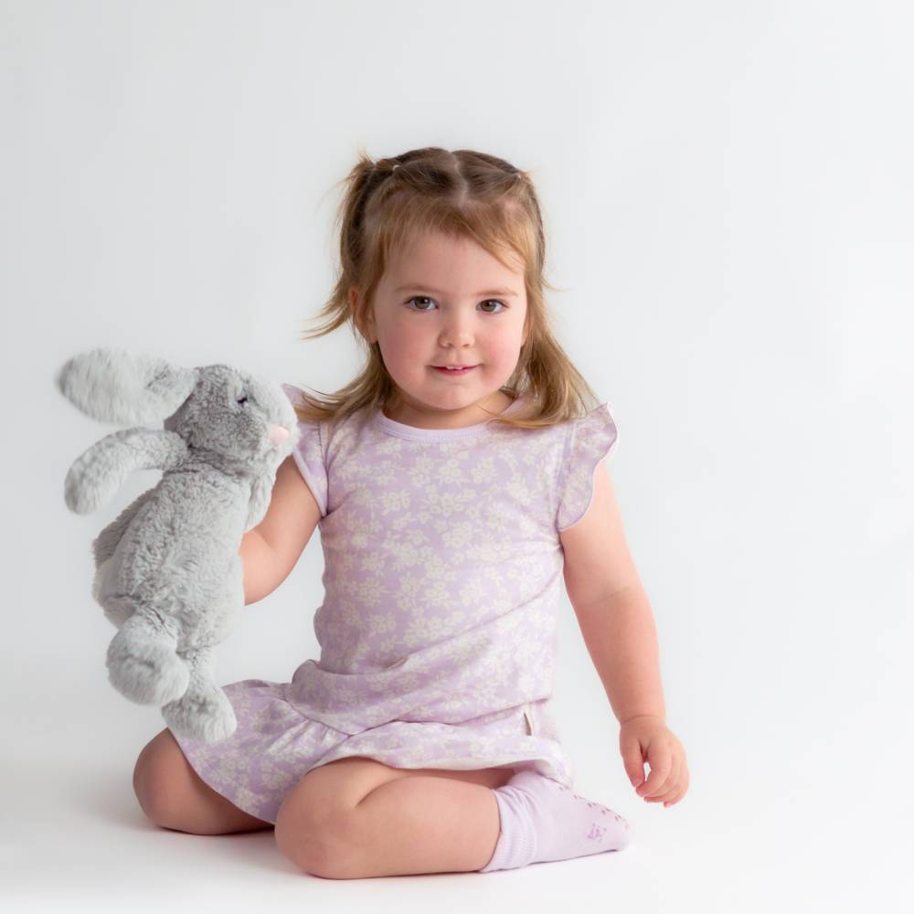 Child in a purple nightdress holding a gray plush toy on a white background