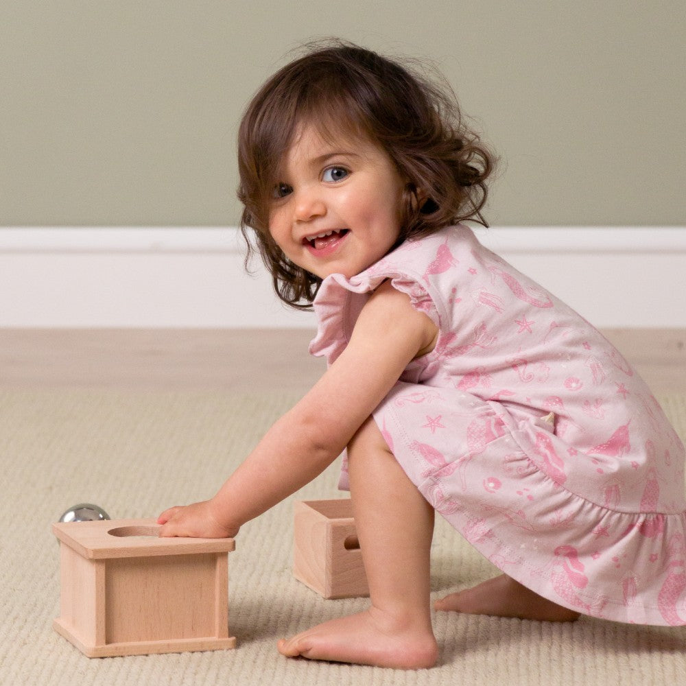 Child in a pink night dress playing with wooden toys on a beige carpet.
