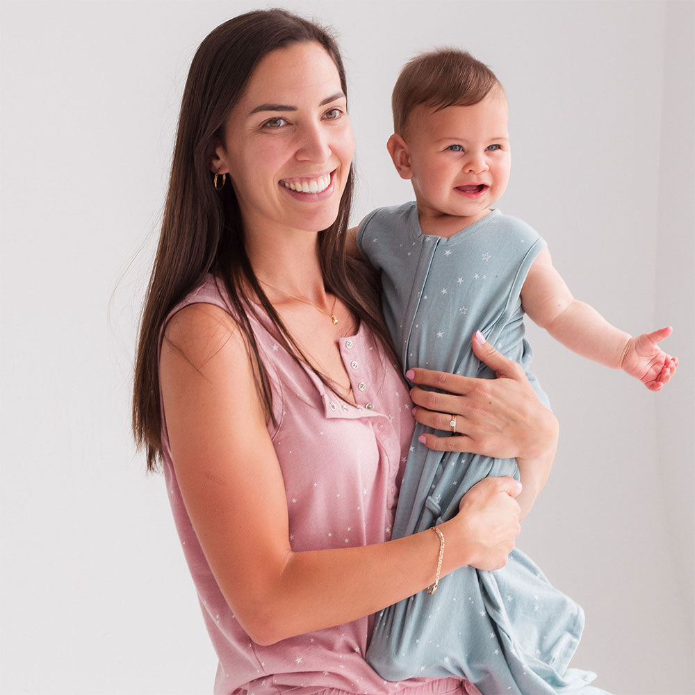 Woman holding a baby wrapped in a light blue swaddle against a plain background