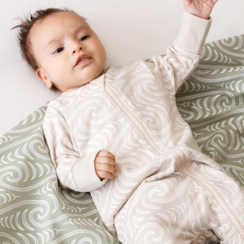 Baby lying on a patterned surface wearing a white swaddle with a subtle design.