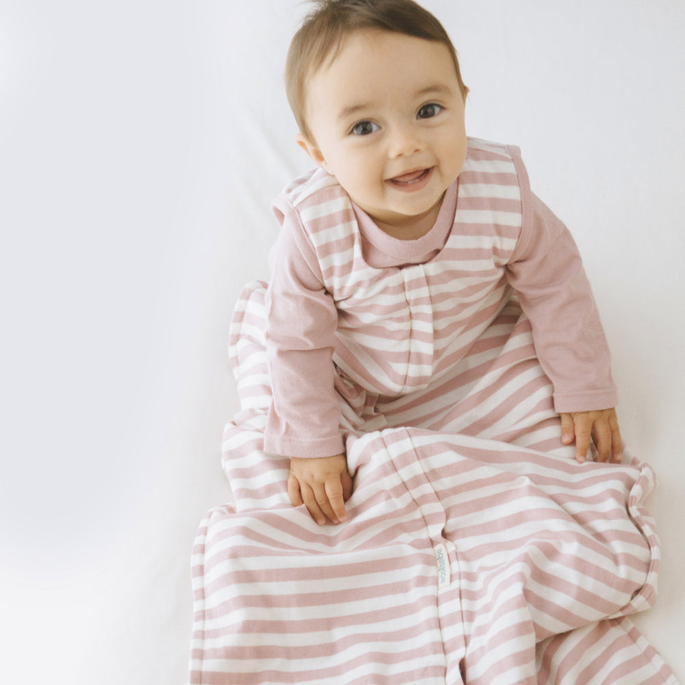 Baby wearing a pink and white striped Dusk Woolbabe sleep sack on a plain background