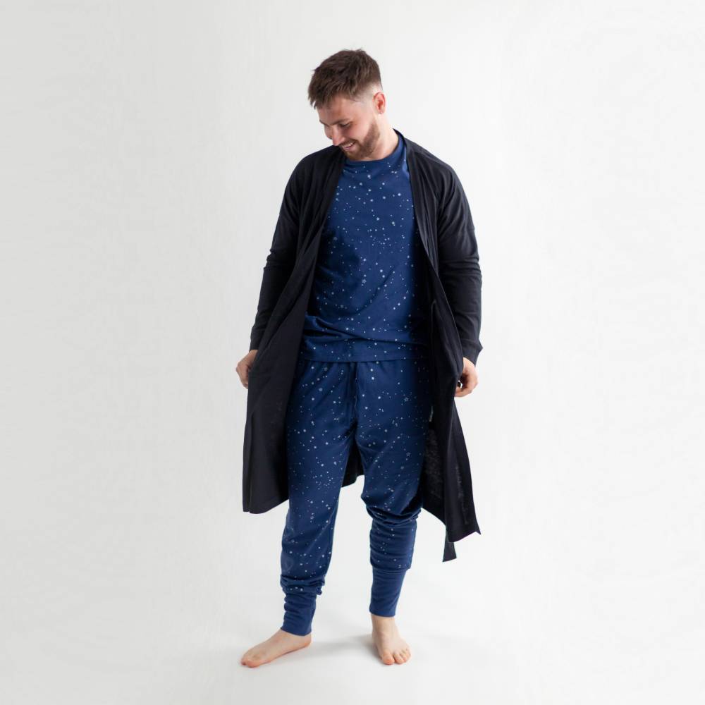 Man wearing a navy blue pajama set with a long dark jacket on a white background