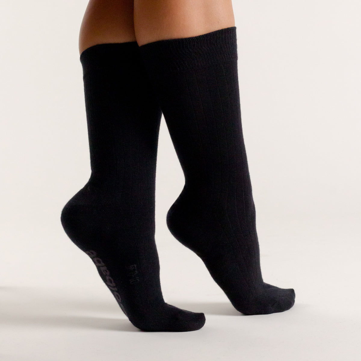 Black merino cotton woolbabe socks worn by a person on a light gray background