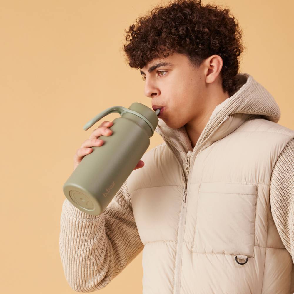 Person drinking from a green water bottle against a beige background