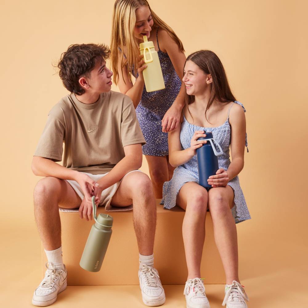 Three people sitting on a bench holding colorful water bottles against a beige background