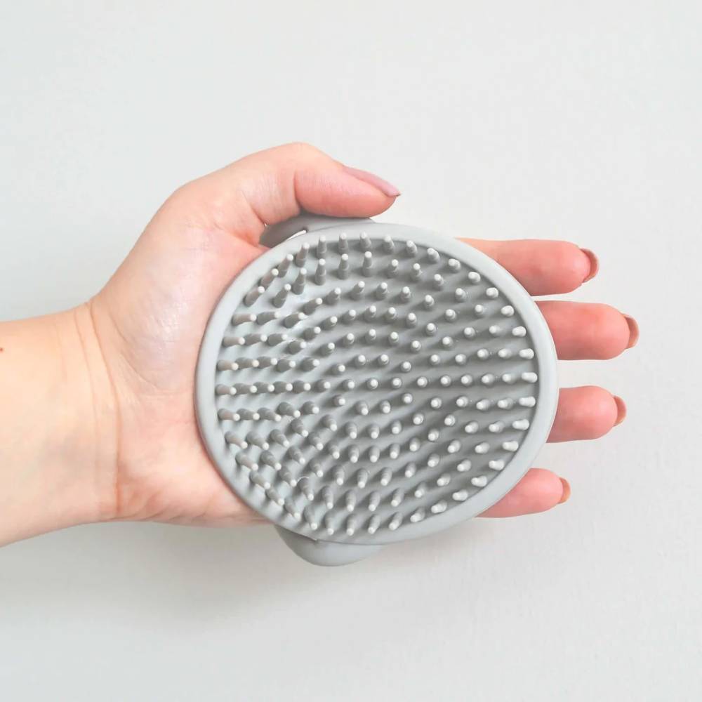 Hand holding a gray silicone brush with textured surface on a light gray background