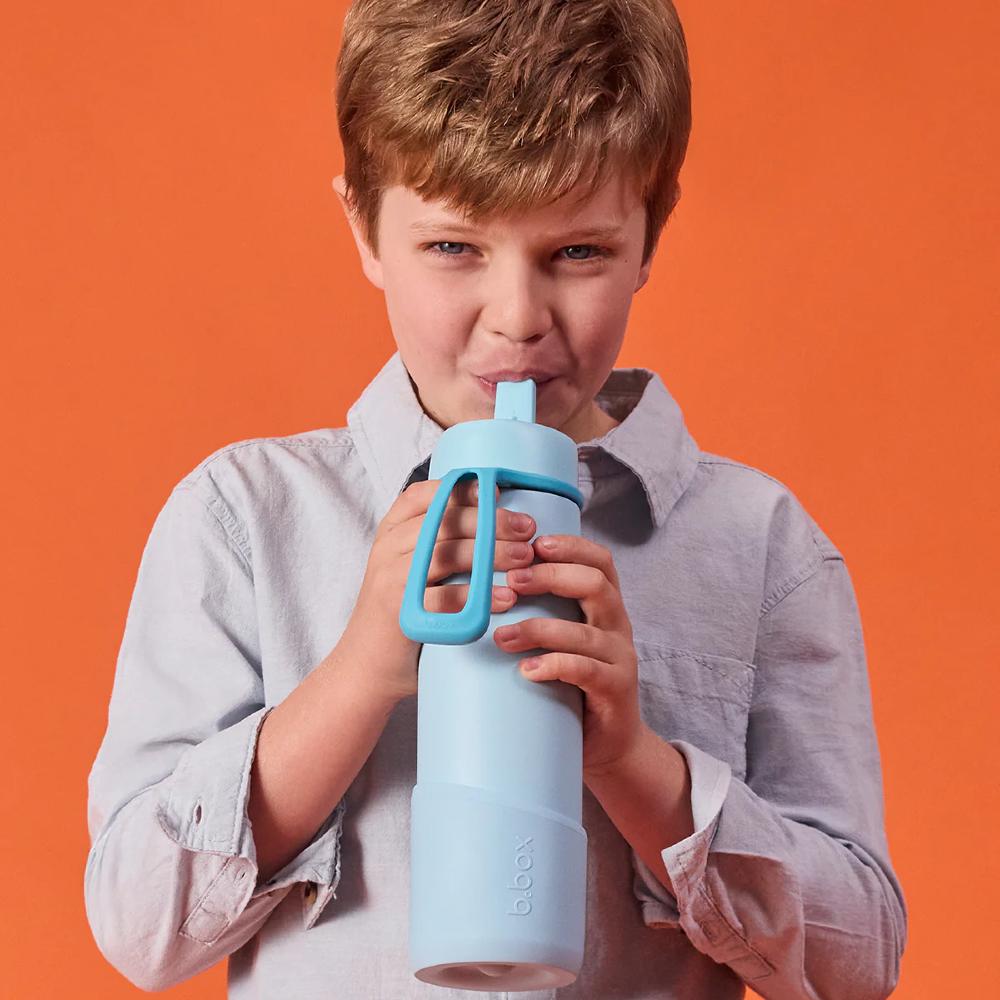 Child holding a light blue water bottle with a straw on an orange background