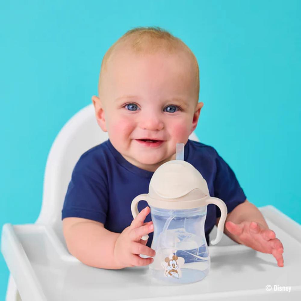 Baby sitting in a high chair holding a sippy cup with a blue background