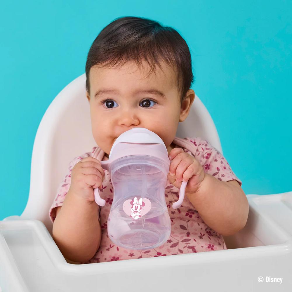 Baby in a high chair holding a pink sippy cup against a blue background