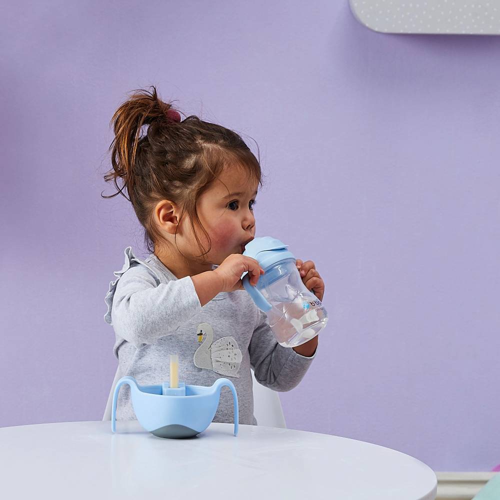 Child drinking from a blue sippy cup with a purple background