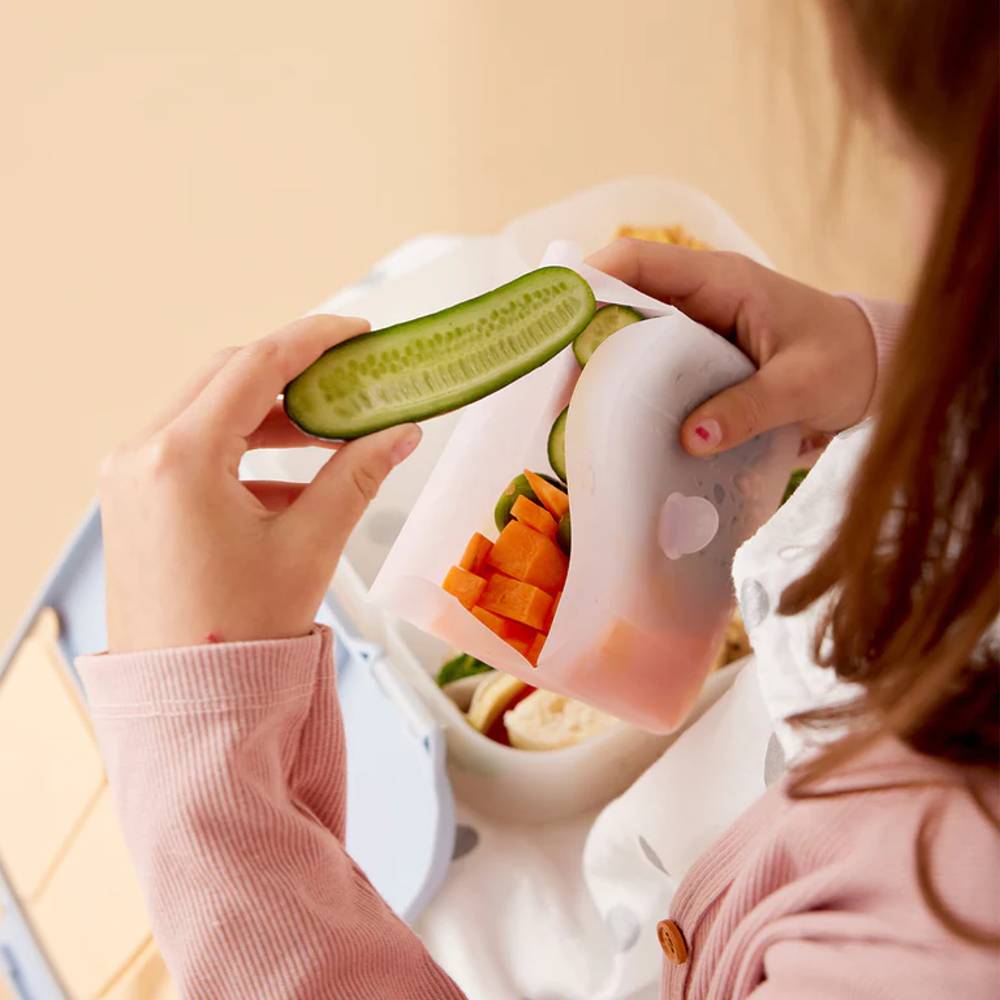 Person holding a sliced cucumber over a container of food.