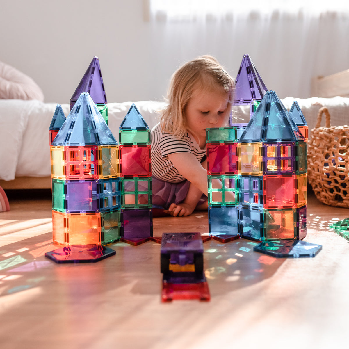 Child playing with colorful magnetic building blocks on a wooden floor.