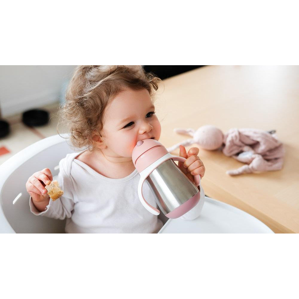 Child holding a pink and silver sippy cup indoors