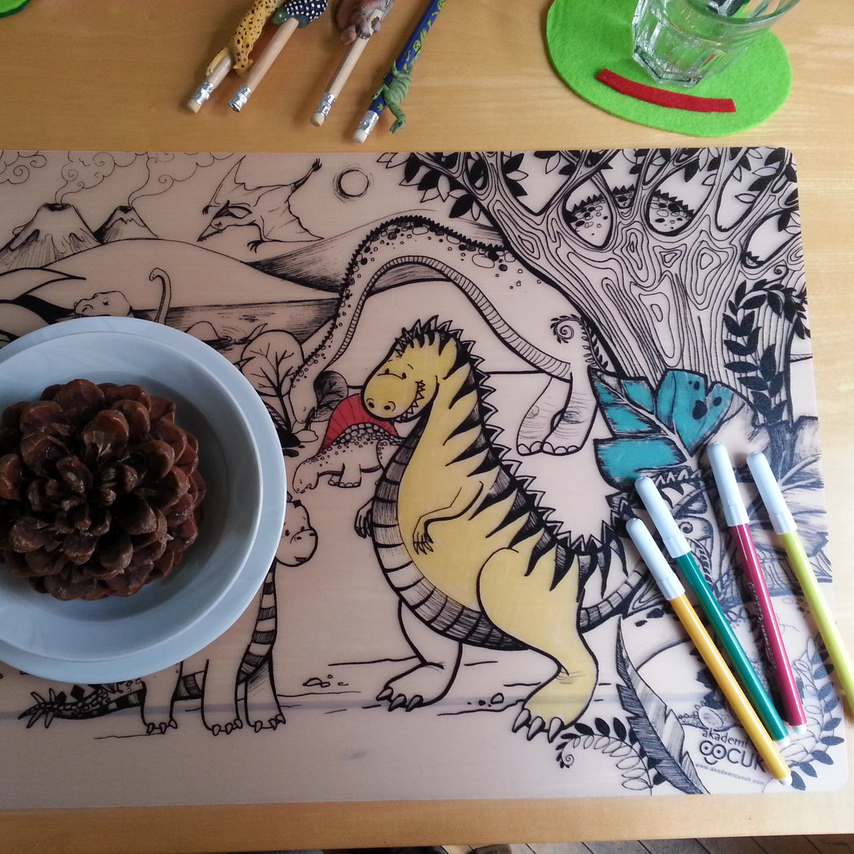 Reusable Colouring Mat - Jurassic Age coloured in with felts on top, a pinecone and glass above