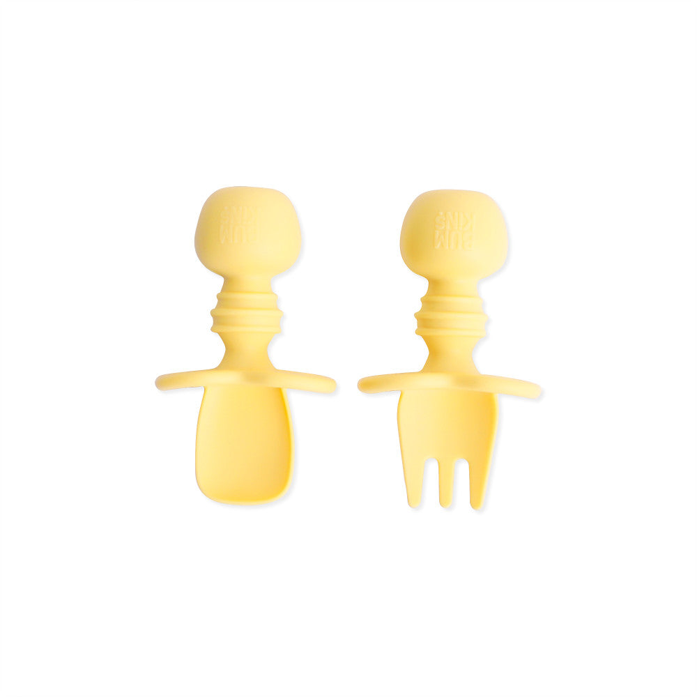 A yellow set of silicone baby cutlery chewtensils including one spoon and one fork with bumkins logo on the handle