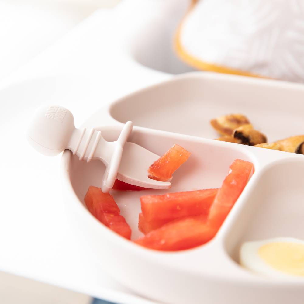A close up of a sand beige coloured chewtensil fork picking up watermelon in a bumkins grip dish 