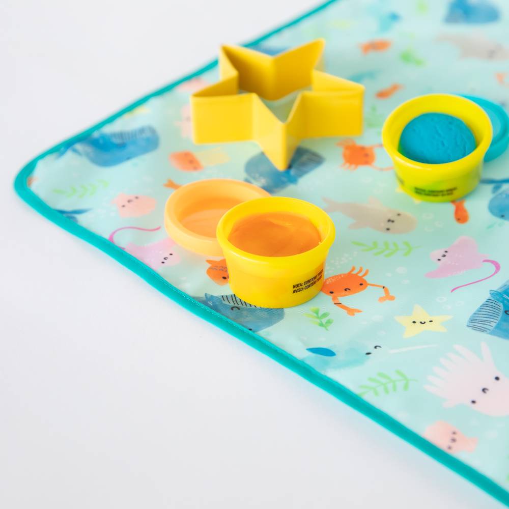 A close up of the blue, ocean theme splat mat with orang and blue play-doh and yellow star cutter on top