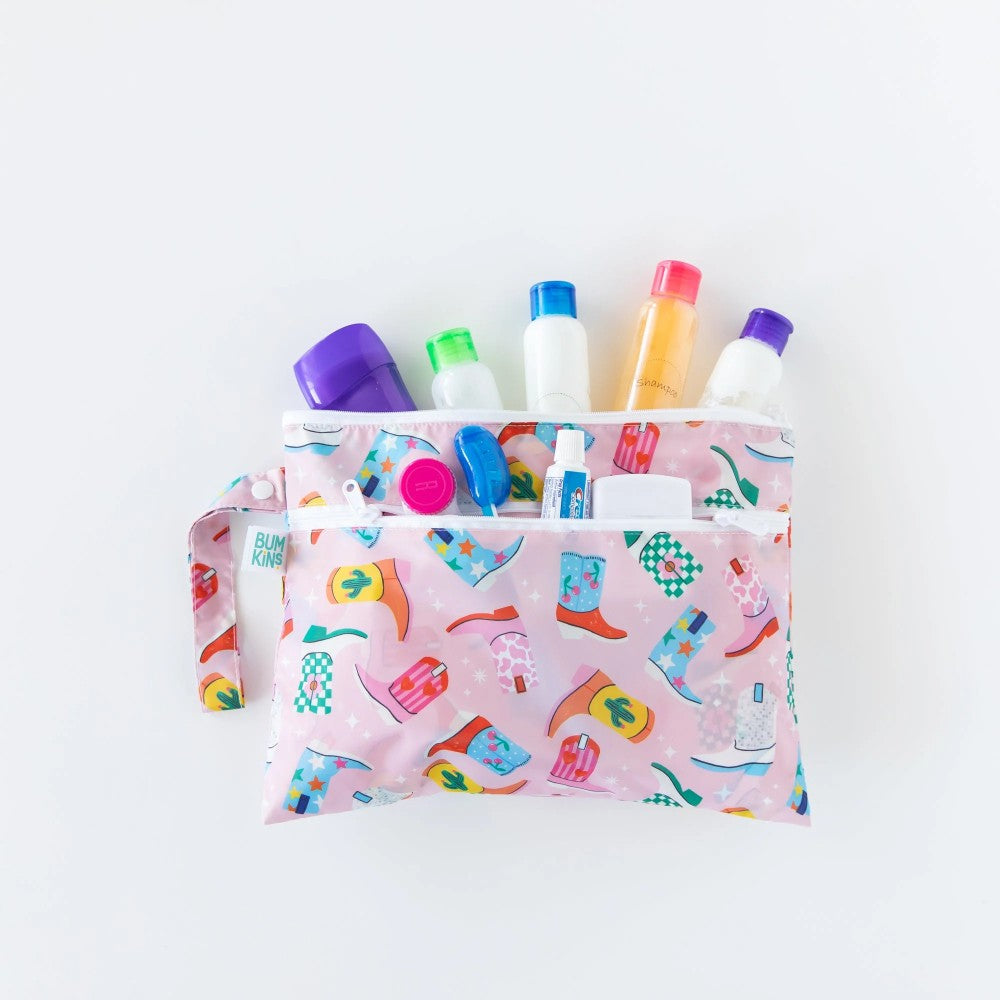 Various toiletries arranged inside both sections of a light pink wet and dry clutch multi-coloured boot pattern on a white background