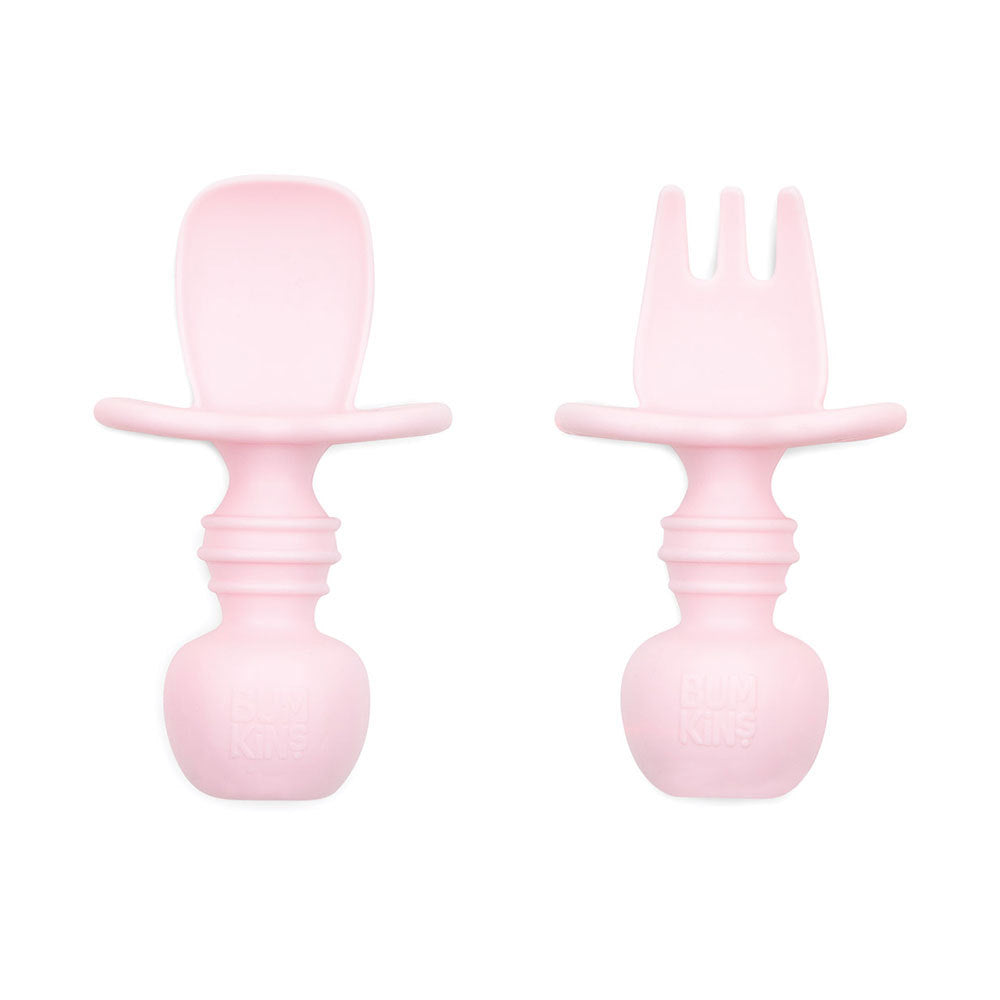 An light pink set of silicone baby cutlery chewtensils including one spoon and one fork with bumkins logo on the handle
