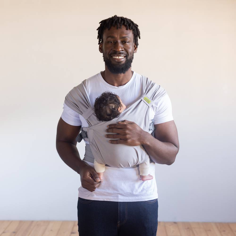 Man holding a baby in a carrier against a plain background