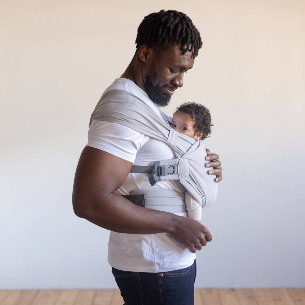 Man holding a child in a baby carrier against a plain background