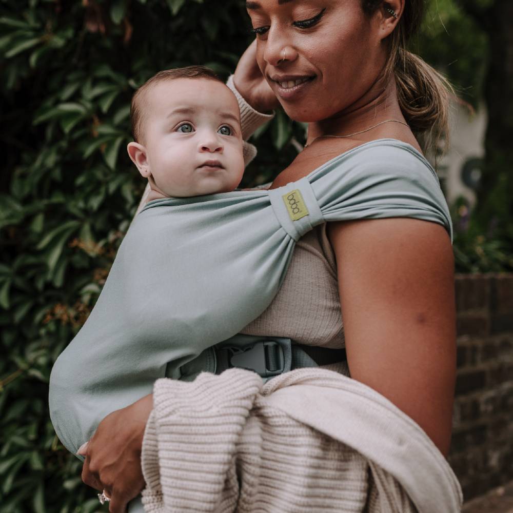 Woman holding a baby in a green sling against a natural background